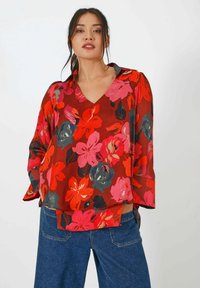 Rode bloemenblouse met een V-hals, brede mouwen en levendige roze en blauwe bloempatronen op een transparante textuur. Gecombineerd met denim.