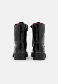 Bottines en cuir verni noir avec une finition brillante, dotées d'une fermeture éclair, d'une doublure rouge et d'une semelle noire épaisse. Marque "TOM TAILOR" visible.
