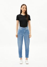 Zwart T-shirt met korte mouwen gecombineerd met lichtblauwe, high-waisted jeans. De jeans hebben een losse pasvorm en zijn omgeslagen bij de enkels. Witte sneakers.