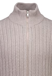 Ljust beige zip-sweater med hög krage, har en ribbad textur och ett fiskbensmönster, avslutad med en silverdragkedja.