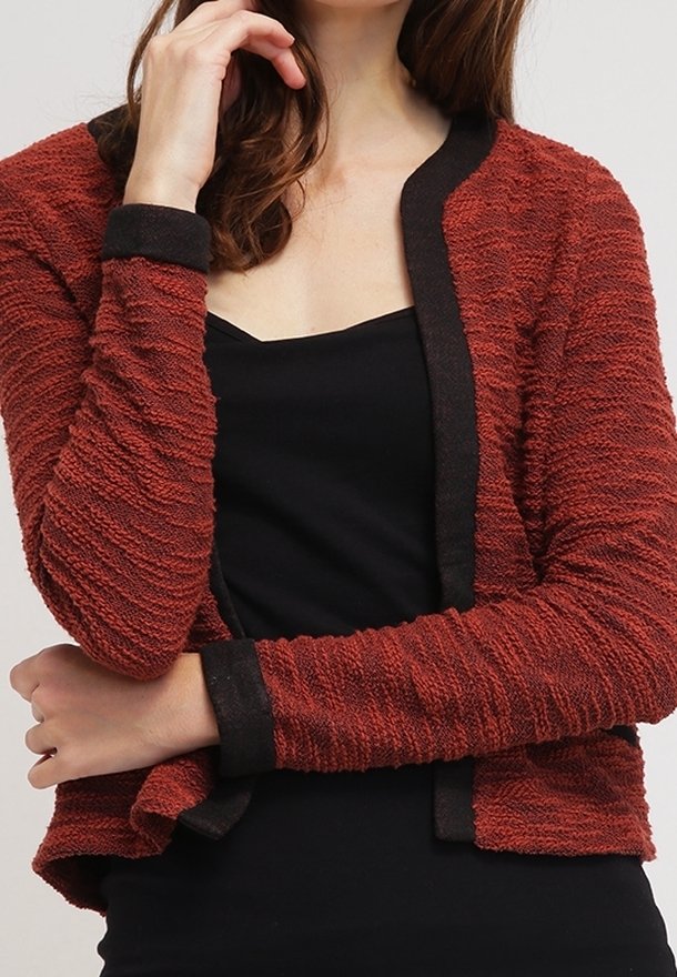 Rød tekstureret cardigan med en sort kant, med rund hals og åben front, iført over en sort top.