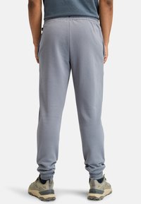 Hellgraue Jogginghose mit elastischem Bund und bündchenartigen Abschlüssen. Verfügt über seitliche Taschen und eine glatte, weiche Textur. Getragen mit beigen Turnschuhen.