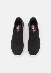 Zwarte instapsneakers met een ademende gebreide bovenkant, textielstof en een witte rubberen zool. Voorzien van paarse branding aan de binnenkant van de schoen.