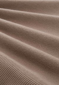 Weiches braunes Gewebe mit feiner Stricktextur und einem gerippten Detail entlang des Randes, nahaufnahme der Falten gezeigt.