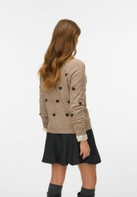 Brauner Strickpullover mit schwarzen Herzmustern, mit Spitzenbesatz an den Ärmeln, kombiniert mit einem dunkelgrauen, ausgestellten Rock.