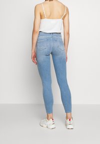 Ljusblå högmidjade jeans med en figursydd design, som har bakfickor och minimal blekning, i kombination med en vit linne och sneakers.