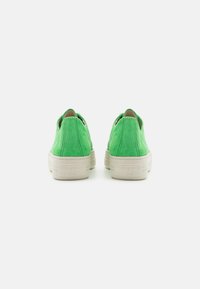 Scarpe slip-on in suede verde vivace con una suola testurizzata color crema. Presentano un design minimale senza lacci visibili e un dettaglio del logo sul tallone.