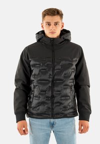 Abrigo acolchado negro con un diseño acolchado, que incluye capucha, cierre delantero y bolsillos laterales; textura suave con una mezcla de materiales mate y brillantes.