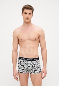 Fekete boxer alsónadrág fehér margarétás mintával, zöld középponttal, texturált anyagból, fekete derékrésszel, rajta "HUGO" felirattal.