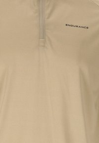 Tissu beige texturé avec une courte fermeture éclair verticale et le logo "ENDURANCE" imprimé en noir sur le côté supérieur droit.