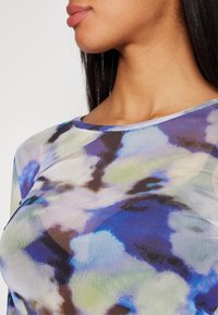 Genomskinlig topp i en blandning av blå, grön och brun abstrakt mönster med rundad halsringning och en slät textur som framhäver det mjuka tygets fall.