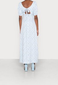 Modrá květinová maxi šaty s nabíranými rukávy, designem na zavazování vzadu a vzorovanou látkou. Spárováno se světle modrými botami na blokovém podpatku.