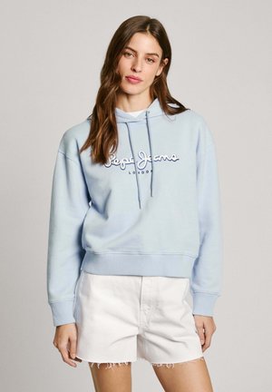 Felpa azzurra con cappuccio e lacci, con logo frontale, abbinata a pantaloni corti di jeans bianchi con orli sfilacciati. Tessuto morbido, vestibilità rilassata.