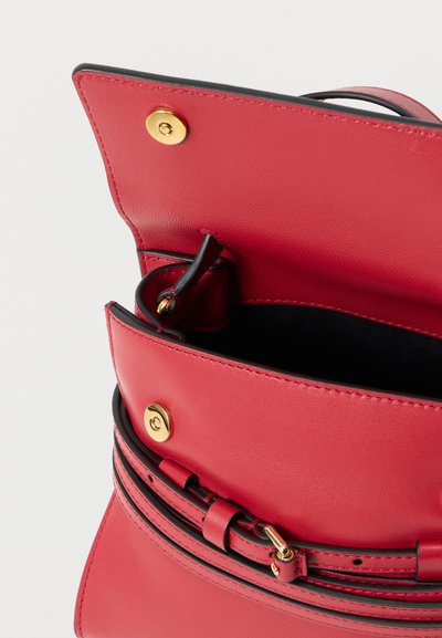 Κόκκινη δερμάτινη τσάντα χειρός με χρυσά κουμπώματα και ρυθμιζόμενο λουρί, ανοιχτή για να αποκαλύψει το μαύρο εσωτερικό επένδυμα.
