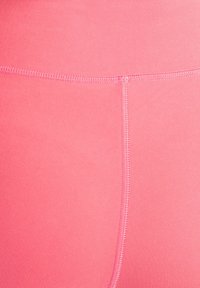 Roze leggings met een gladde textuur, voorzien van een elastische tailleband en zichtbare stiksels langs de naden. Close-up van de stof.