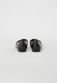 Ballerine in pelle nera con finitura liscia, caratterizzate da un'ornamentazione decorativa lungo la parte posteriore e una suola bassa.
