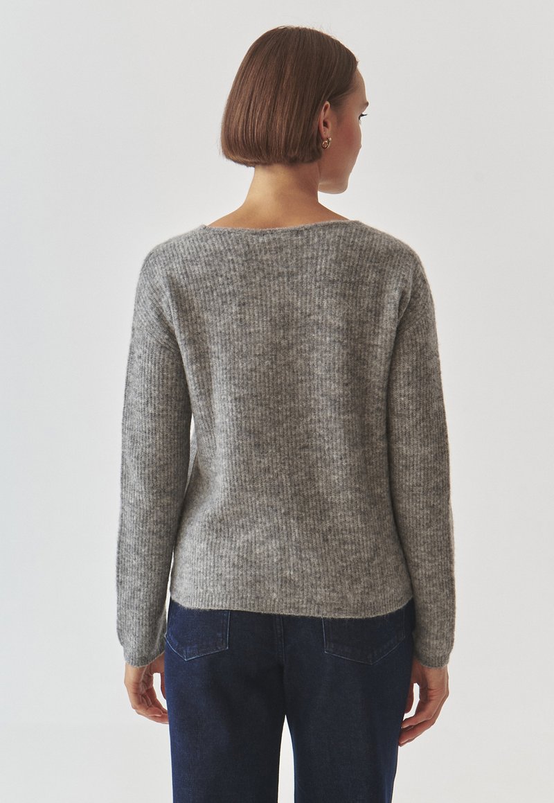 Szary dżersejowy sweter o żeberkowanej fakturze, z szerokim dekoltem i długimi rękawami. Noszony na ciemnych dżinsach, prezentujący luźny krój.