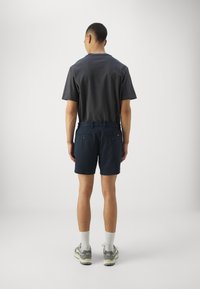 Navy shorts with a smooth texture and two back pockets. Paired with a fitted, dark gray, crew neck t-shirt. Features athletic shoes and socks.