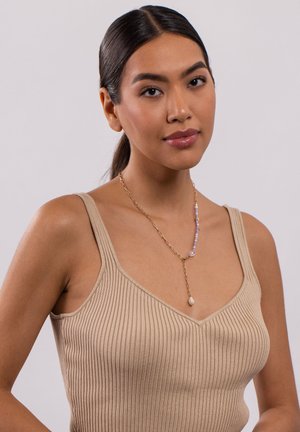 Goldene Halskette mit lila Perlen und einem tropfenförmigen Perlenanhänger, getragen über einem beigen gerippten Tanktop.