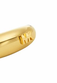 Kullattu metalliosa, jossa on kiillotettu pinta ja kohokuvioitu "MX"-logo. Pyöreä muoto esitellee tyylikkyyttä ja modernia muotoilua.