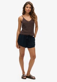 Débardeur tricoté brun avec un motif texturé, associé à un short bleu marine avec un cordon de serrage. Le modèle porte des sandales brunes.