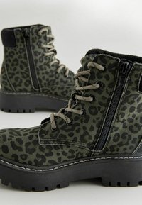 Stivali alla caviglia con stampa leopardata verde e accenti neri, con lacci davanti, cerniera laterale e suola nera spessa. Tessuto morbido e costruzione robusta.