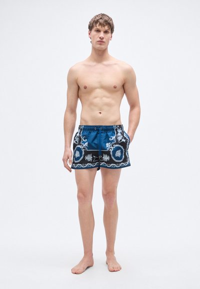 Ανδρικό μαγιό σορτς σε μπλε με μαύρες λεπτομέρειες. Το ύφασμα είναι λείο με περίτεχνα ασημένια σχέδια. Διαθέτει πλαϊνές τσέπες και ελαστική μέση με κορδόνι.