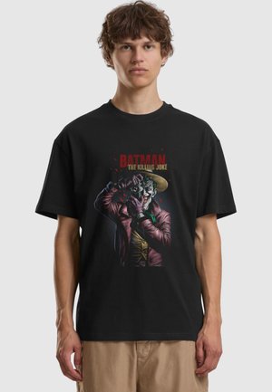 Young man wearing black Batman-themed t-shirt featuring Joker holding a camera, with text "Batman The Killing Joke."