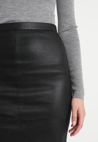 Schwarzer Leder-Bleistiftrock mit glatter Textur, hoher Taille und Nahtdetails, kombiniert mit einem grauen ribbed Langarmtop.