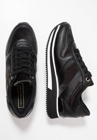 Černé tenisky s kombinací hladkých a strukturovaných materiálů, bílou podr�ážkou, zlatými akcenty a klasickým šněrováním.