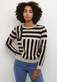 Pull beige avec des rayures noires verticales et horizontales, col rond, manches longues, et poignets et ourlet côtelés. Texture en tricot douce.
