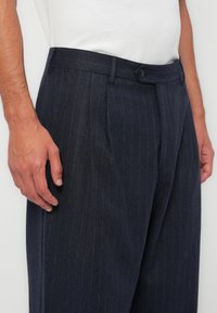 Navy pinstriped trousers made of textured fabric, featuring a button closure, belt loops, and a relaxed fit with sharp pleats.