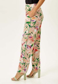 Floral print trousers with a light pink background, featuring vibrant green leaves and multi-colored flowers, elastic waistband, and side pockets.