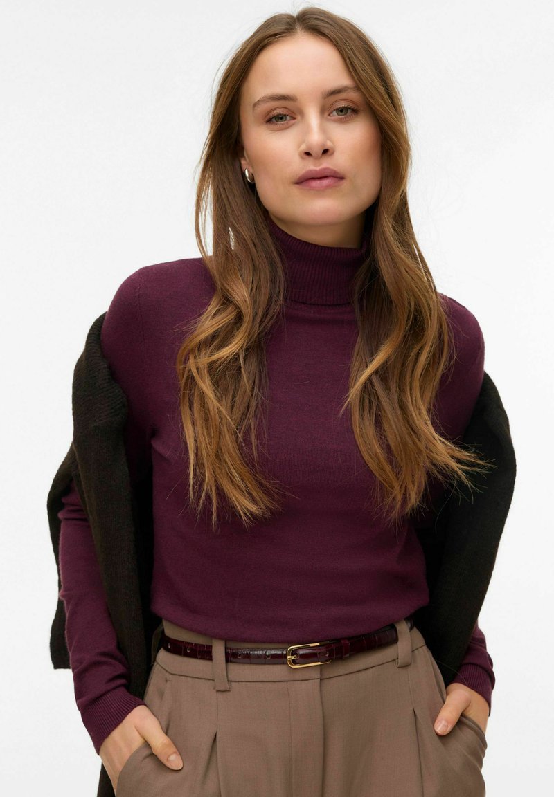 Burgundia värvi poolkaelusega pehme materjaliga kampsun, mida on kombineeritud tumeda kardiganiga, beežide kõrge vöökohaga pükstega ja pruun vöö kuldse pandlaga.