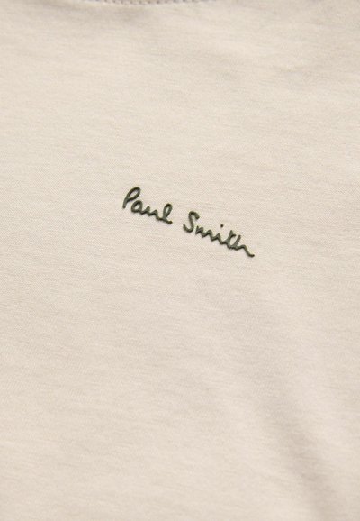 Camiseta de algodón beige con cuello redondo y un logo en cursiva verde de "Paul Smith" en el lado izquierdo. Textura suave y diseño simple.