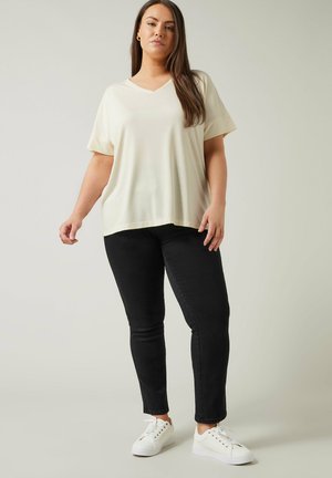 Kortærmet, V-hals, cremetop der er kombineret med sorte skinny jeans og hvide sneakers. Toppen har en afslappet pasform og blød tekstur.