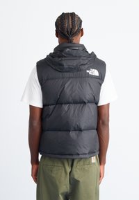 Black puffer vest with a hood, featuring stitched sections for insulation, logo on the back, and a smooth, shiny texture.