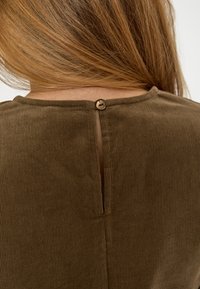 Braunes Cordtop mit rundem Ausschnitt, Knopfverschluss auf der Rückseite und einem kleinen Ausschnitt unter dem Knopf für Belüftung.