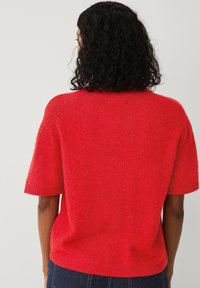 Rød strikket sweater, kortærmet, afslappet pasform, struktureret stof med subtil glans, ribbestrikket hals og ærmer, vist fra ryggen.