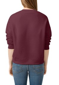 Sweat-shirt bourgogne avec un col rond, coupe ample, poignets côtelés et ourlet côtelé. Associé à un jean bleu ajusté, mettant en avant un design décontracté.