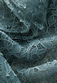 Tissu en dentelle bleue avec des motifs floraux complexes, présentant une surface délicate et texturée ainsi qu'une apparence douce et transparente.