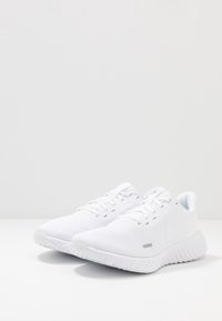 Zapatillas deportivas blancas con una parte superior de malla texturizada, puntera redonda, cordones planos y una suela acolchada. Detalle del logo en el lateral.
