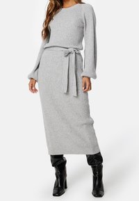 Robe en tricot côtelé grise à deux pièces avec des manches longues et une taille nouée, associée à des bottes en cuir noir montantes. Texture lisse et design ajusté.