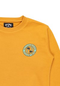 Felpa gialla con un logo rotondo che presenta palme e la scritta "BILLABONG SINCE 1973" in blu, realizzata in un morbido tessuto testurizzato.