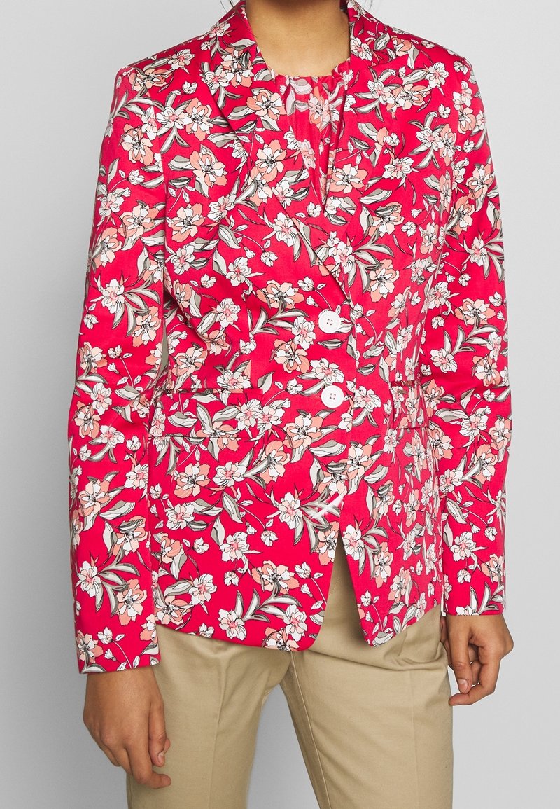 Blommig blazer i klar rosa med krämfärgade, persikofärgade och gröna mönster. Har en skär krage, två knappar och framfickor. Skräddarsydd passform.