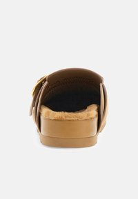 Sandale à glissière marron avec une doublure douce en fausse fourrure, une semelle plate et une bride ajustable dotée d'un accent de boucle dorée. Texture en cuir lisse.