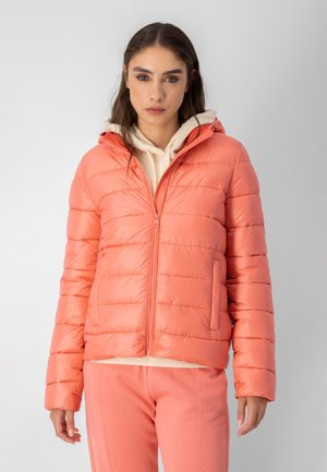 Giacca imbottita color corallo con cappuccio, design trapuntato, zip centrale e tasche laterali. Indossata sopra un hoodie crema e pantaloni della tuta rosa.