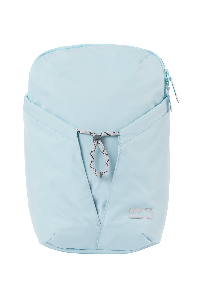 Mochila azul clara con un diseño elegante y curvado, hecha de tela suave. Presenta un bolsillo triangular frontal con cierre de cuerda y una etiqueta de logo.