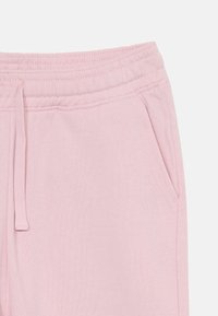 Light pink sweatpants featuring an elastic waistband with drawstring, side pockets, and soft, textured fabric.