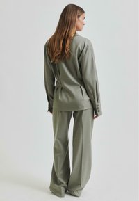 Cămașă verde măsliniu, cu croi lejer, mâneci lungi și manșete cu buton, asortată cu pantaloni largi, amândouă dintr-un material neted.